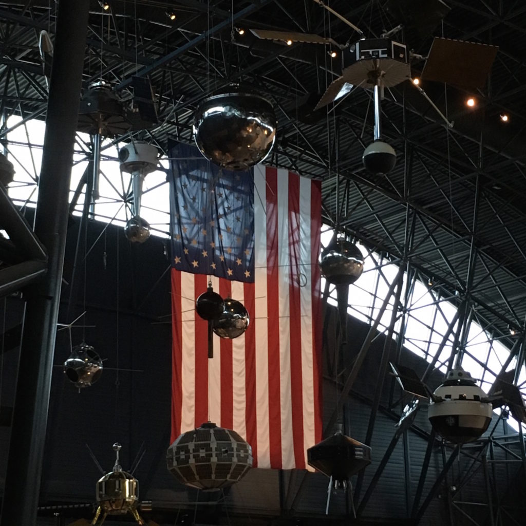 Satellites on display in front of an American flag at the National Air and Space Museum, Steven F. Udvar-Hazy Center